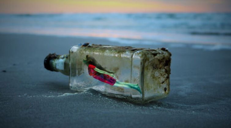 Une bouteille en verre échouée sur le sable au bord de l'eau, contenant une femme à l'interieur, symbolisant l'inspiration et les idées créatives.